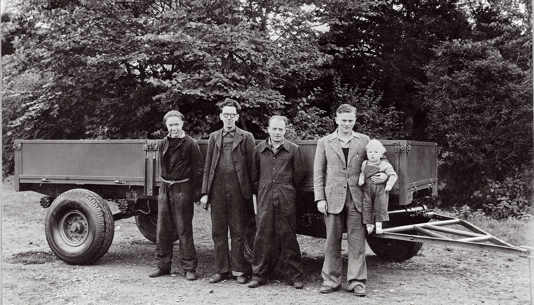 1947. Anthony Bamford en los brazos de su padre. De izquierda a derecha, los empleados Bill Hirst, Arthur Harrison y Bert Holmes...