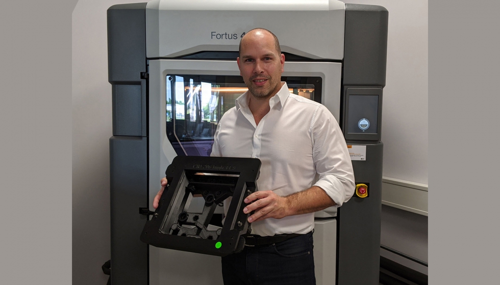 Stefan Kammann frente a la impresora 3D Fortus 450mc en el Centro de competencia ADaM, sosteniendo una gua de pegado conforme con ESD impresa en 3D...