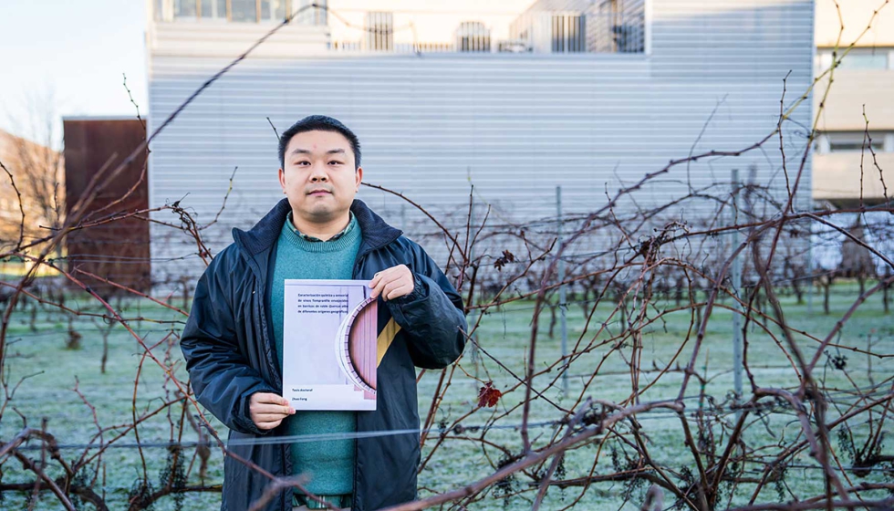 Zhao Feng posa con el volumen de su tesis en los viedos y junto a la bodega experimental de la Universidad de La Rioja